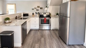 A modern kitchen with stainless steel appliances, a granite countertop, and a wooden floor.