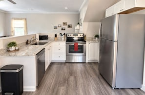 A modern kitchen with stainless steel appliances, a granite countertop, and a wooden floor.