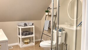 A modern bathroom with a glass shower enclosure, a white toilet, and a shelf with towels.