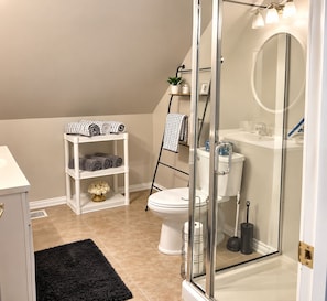A modern bathroom with a glass shower enclosure, a white toilet, and a shelf with towels.