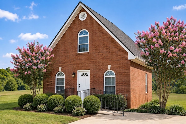 A two-story brick building with a gabled roof, a white front door, and a small porch with a black railing.
