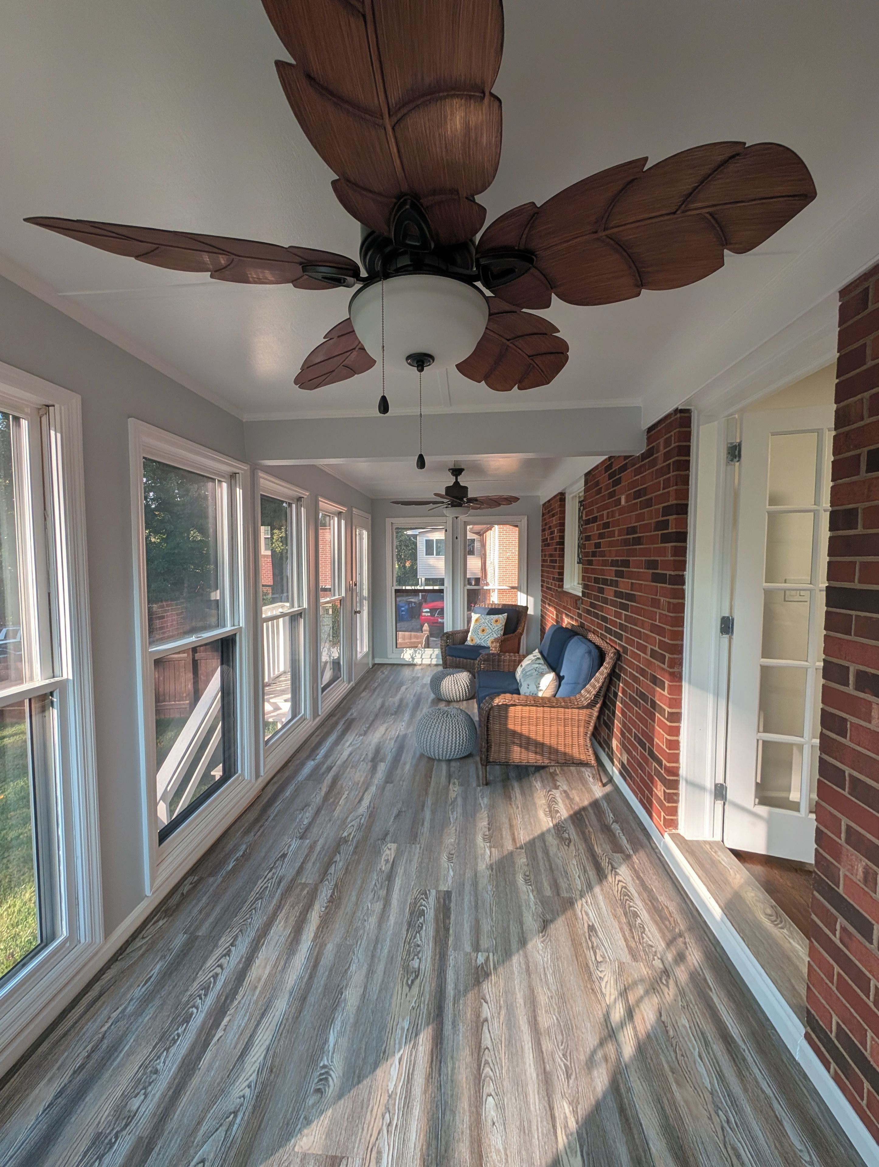 A sunroom with large windows, a ceiling fan, and a brick wall.