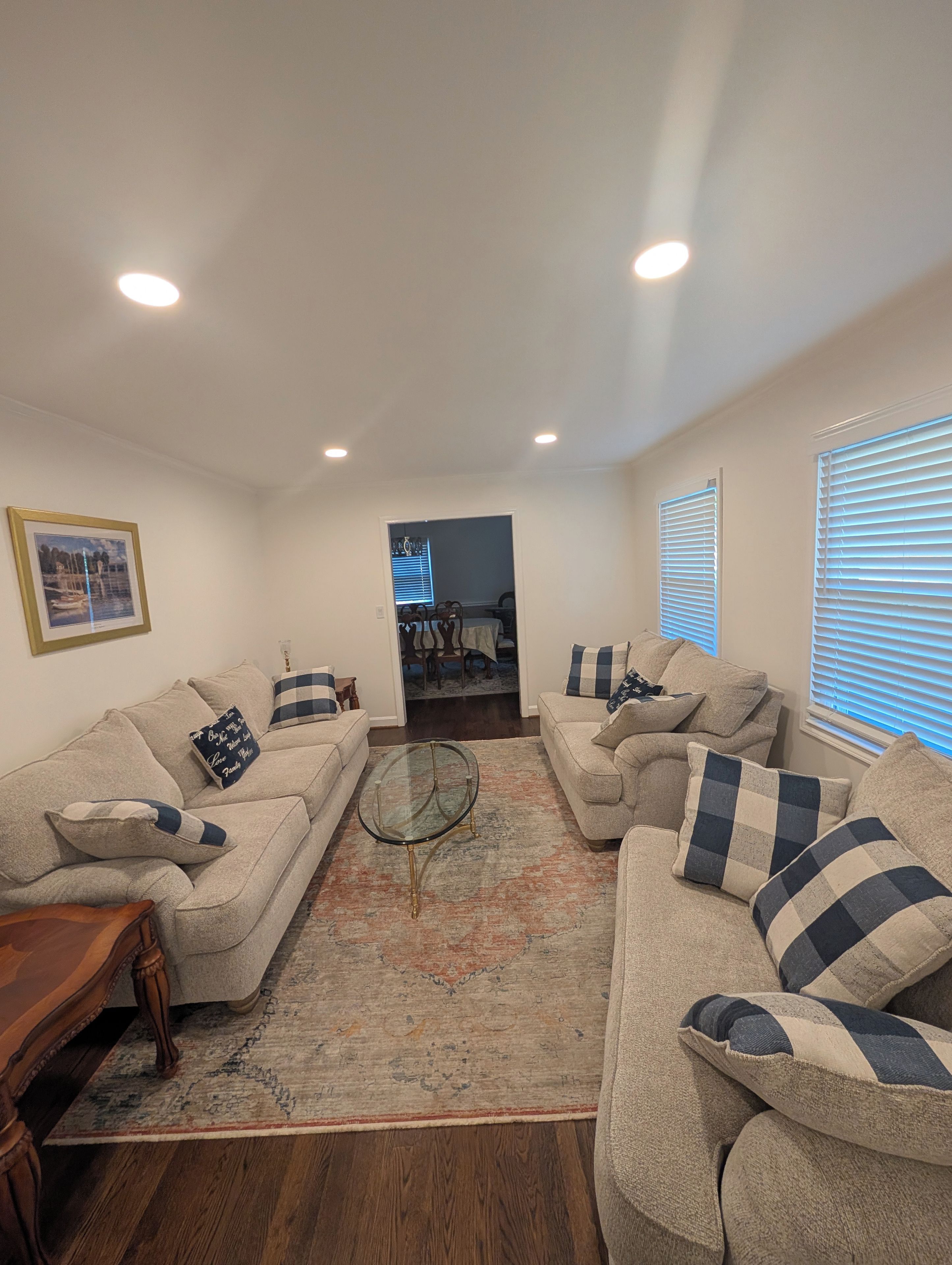 A living room with two sofas, a coffee table, and a rug. There is a dining area visible through an open doorway.