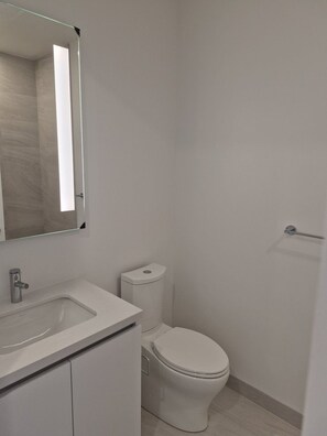 A bathroom with a white sink, mirror, and toilet. - Brand New Studio on LRT Line (Toronto)