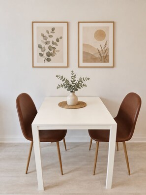 A dining table with two chairs, a vase with a plant, and two framed artworks on the wall. - Brand New Studio on LRT Line (Toronto)