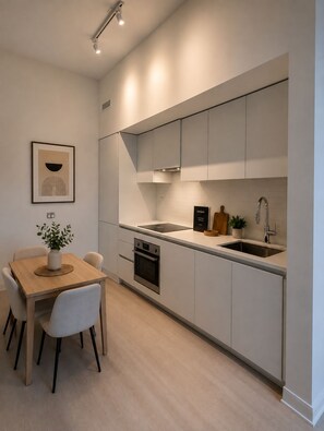 A modern kitchen with white cabinetry, a built-in oven, a sink, and a dining area with a wooden table and chairs. - Brand New Studio on LRT Line (Toronto)