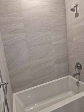 A modern bathroom with a bathtub, shower, and a wall-mounted towel rack. - Brand New Studio on LRT Line (Toronto)