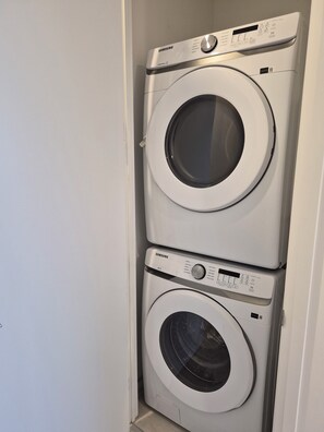 A stacked washer and dryer unit with control panels and a door. - Brand New Studio on LRT Line (Toronto)