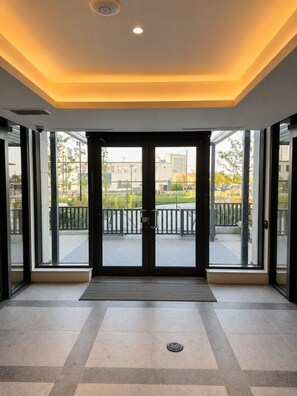 A modern hotel entrance with a glass door, a metal threshold, and a view of the outdoor area. - Brand New Studio on LRT Line (Toronto)