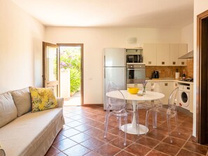 A compact living space with a sofa, a dining table with chairs, a kitchen area with appliances, and a view through an open door. - Casa Dell'Ulivo by Interhome (San Teodoro)