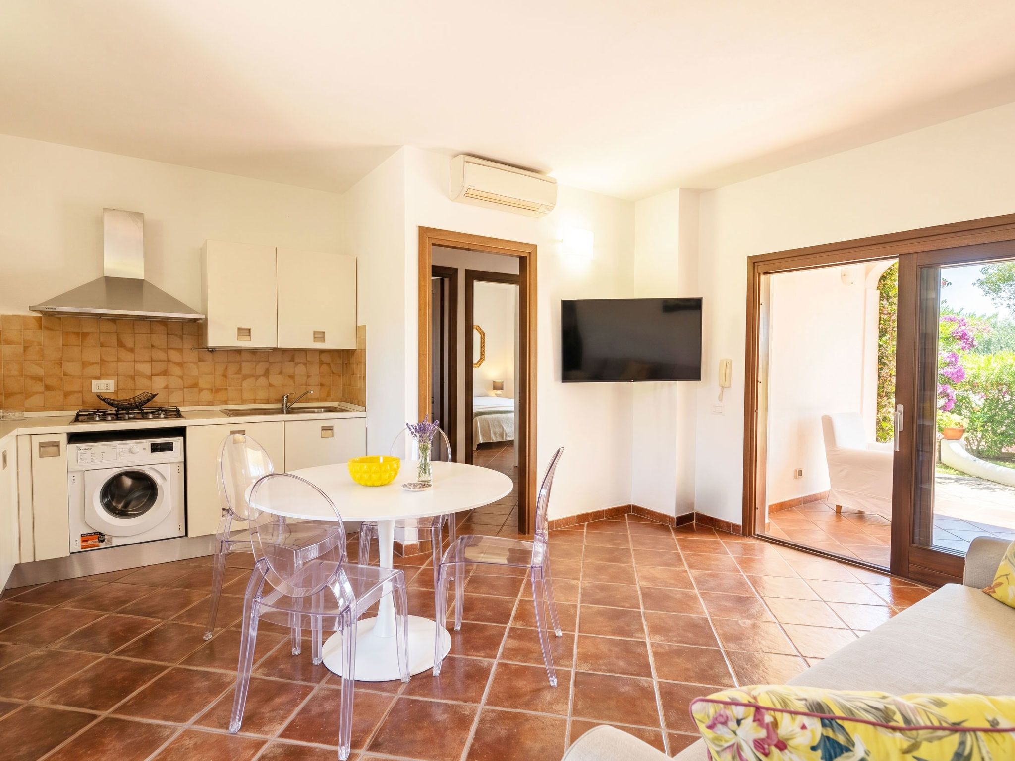 Una cocina moderna con lavadora integrada, un comedor con mesa redonda y sillas, y un televisor montado en la pared.