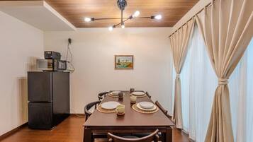 A dining area with a wooden table set for four, a black refrigerator, and a ceiling light fixture.