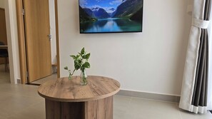 Una habitación con una mesa redonda de madera, una planta en maceta y un televisor de pared que muestra un paisaje pintoresco.