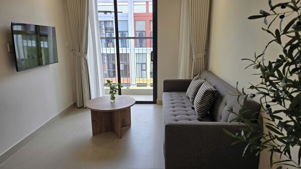 Una sala de estar moderna con un sofá gris, una mesa redonda de madera y un televisor montado en la pared.