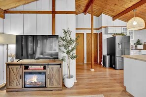 A modern kitchen with a large flat-screen TV, wooden cabinets, and a built-in fireplace. - Cozy Cabin Retreat with Hot Tub & Fire Pit. (Pocono Summit)
