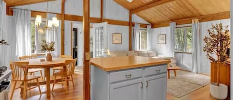 A spacious kitchen with a central island, wooden flooring, and a high ceiling with exposed beams.
