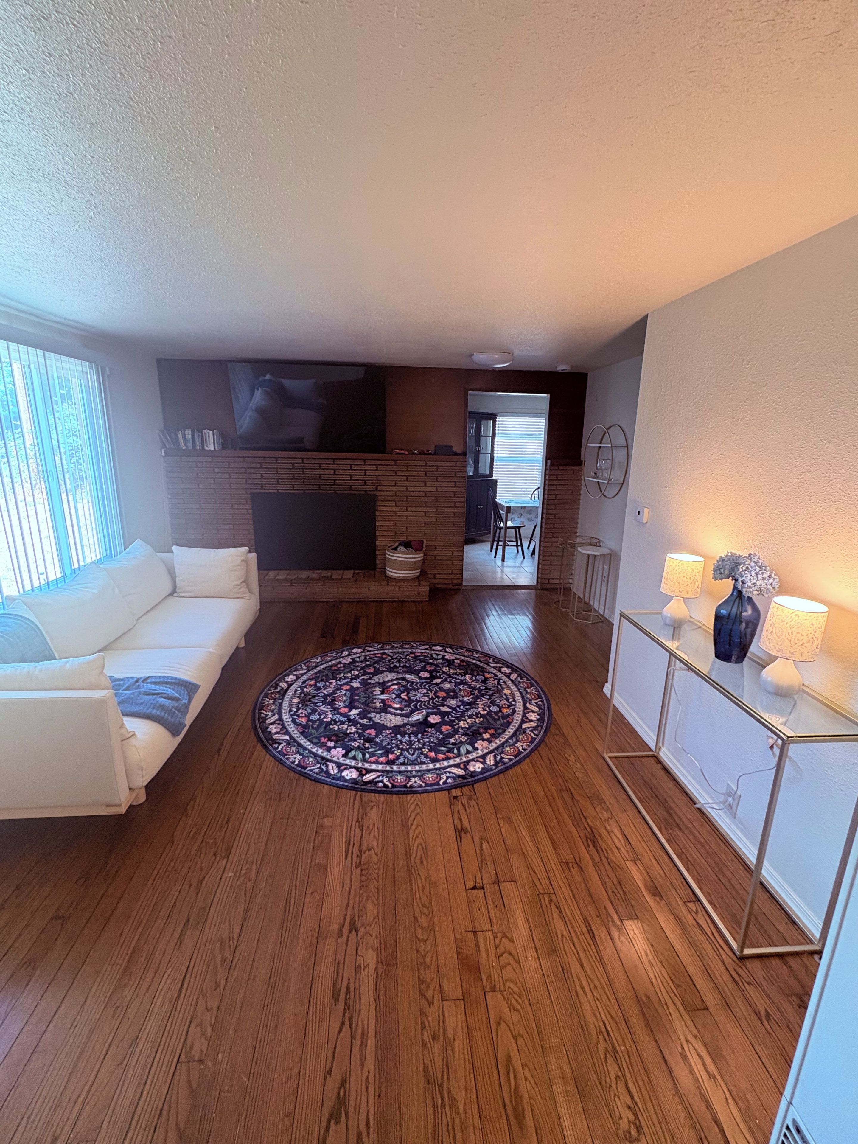Un salon moderne avec un canapé blanc, un tapis à motifs et un téléviseur à écran plat fixé au mur.