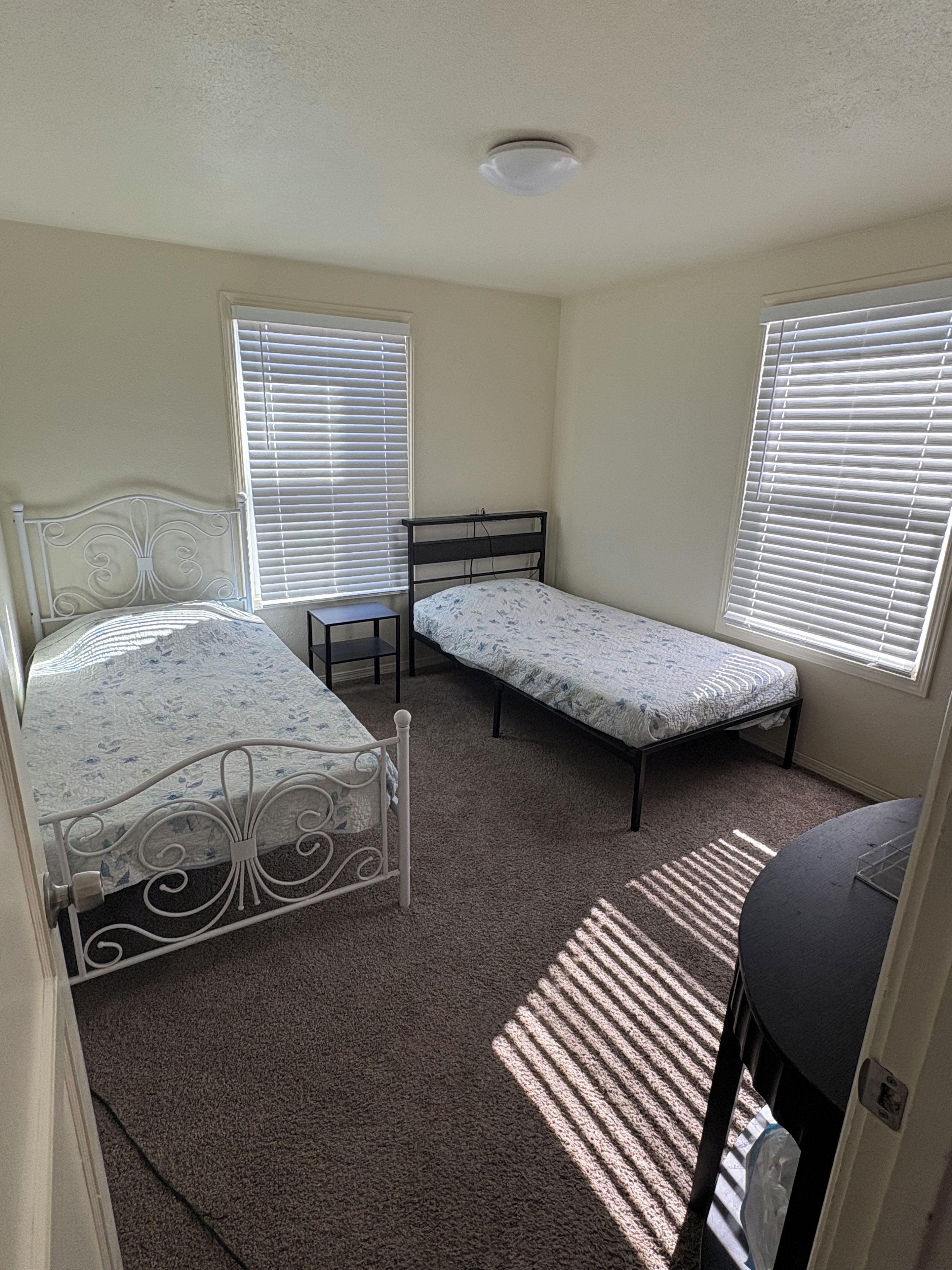 Une chambre avec deux lits, une fenêtre et un luminaire au plafond.