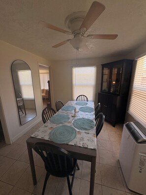 Un coin repas avec une table dressée pour quatre personnes, un ventilateur de plafond et un réfrigérateur.