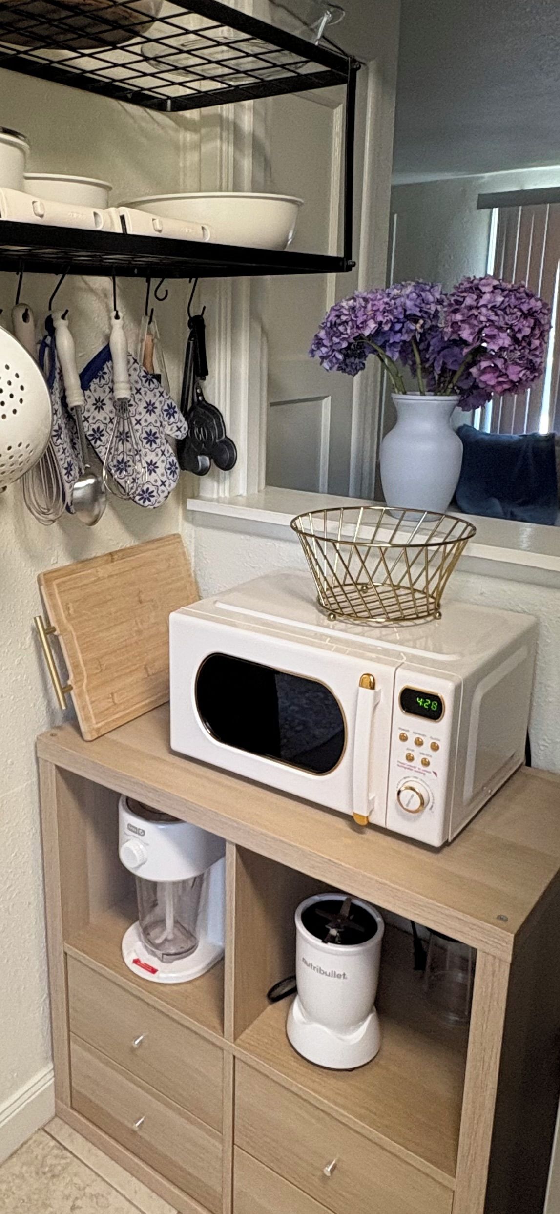 A kitchen with a microwave on a wooden shelf, a coffee maker, and kitchen utensils hanging on the wall.