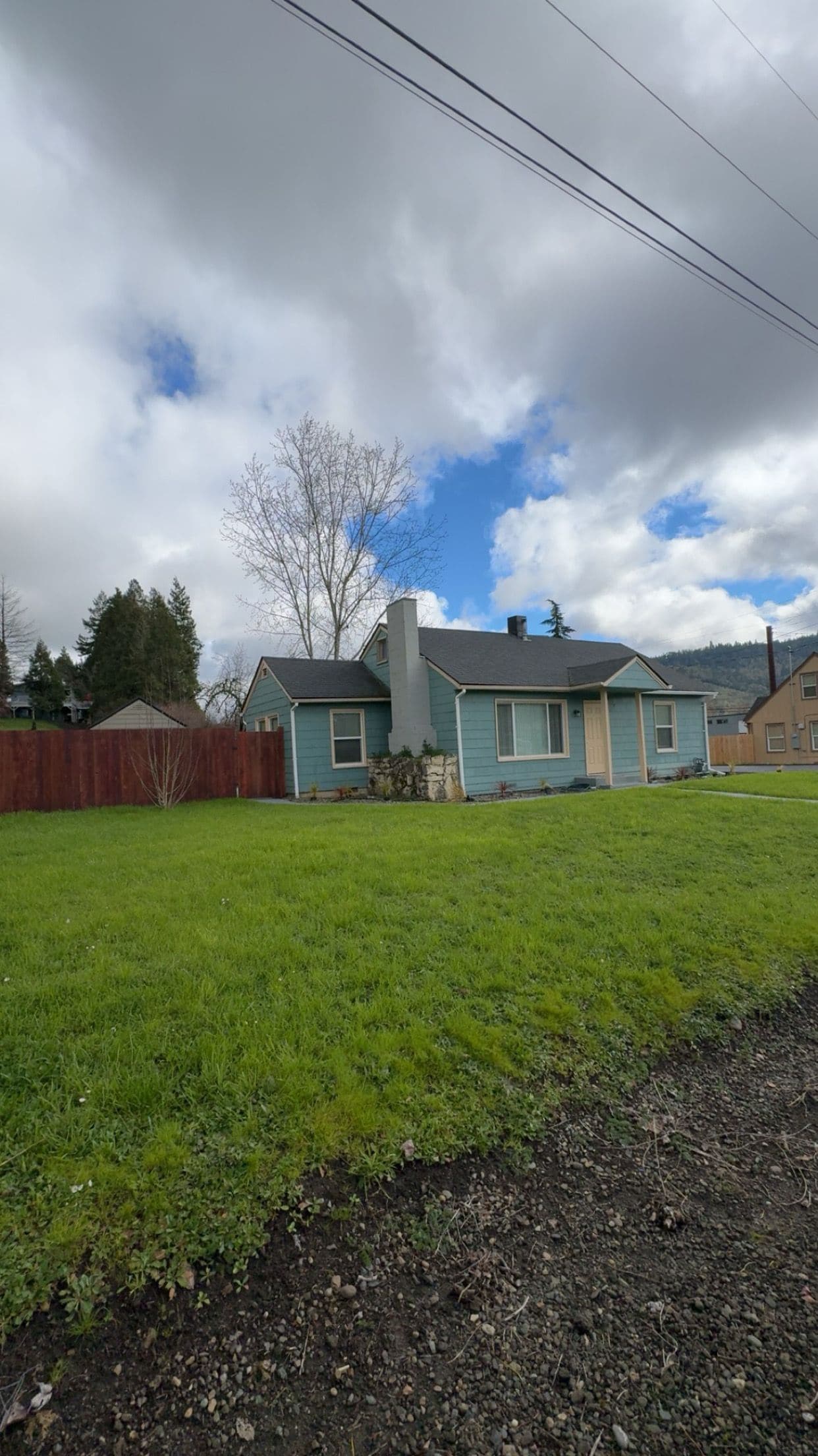 A residential house with a front yard, a wooden fence, and a clear sky.