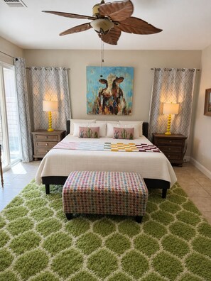 A bedroom with a bed, a ceiling fan, a painting, two bedside tables with lamps, and a green rug. - Redford Villa- 3BR Home + 1BR Private Casita, Pool/Spa, Close to Polo (Indio)