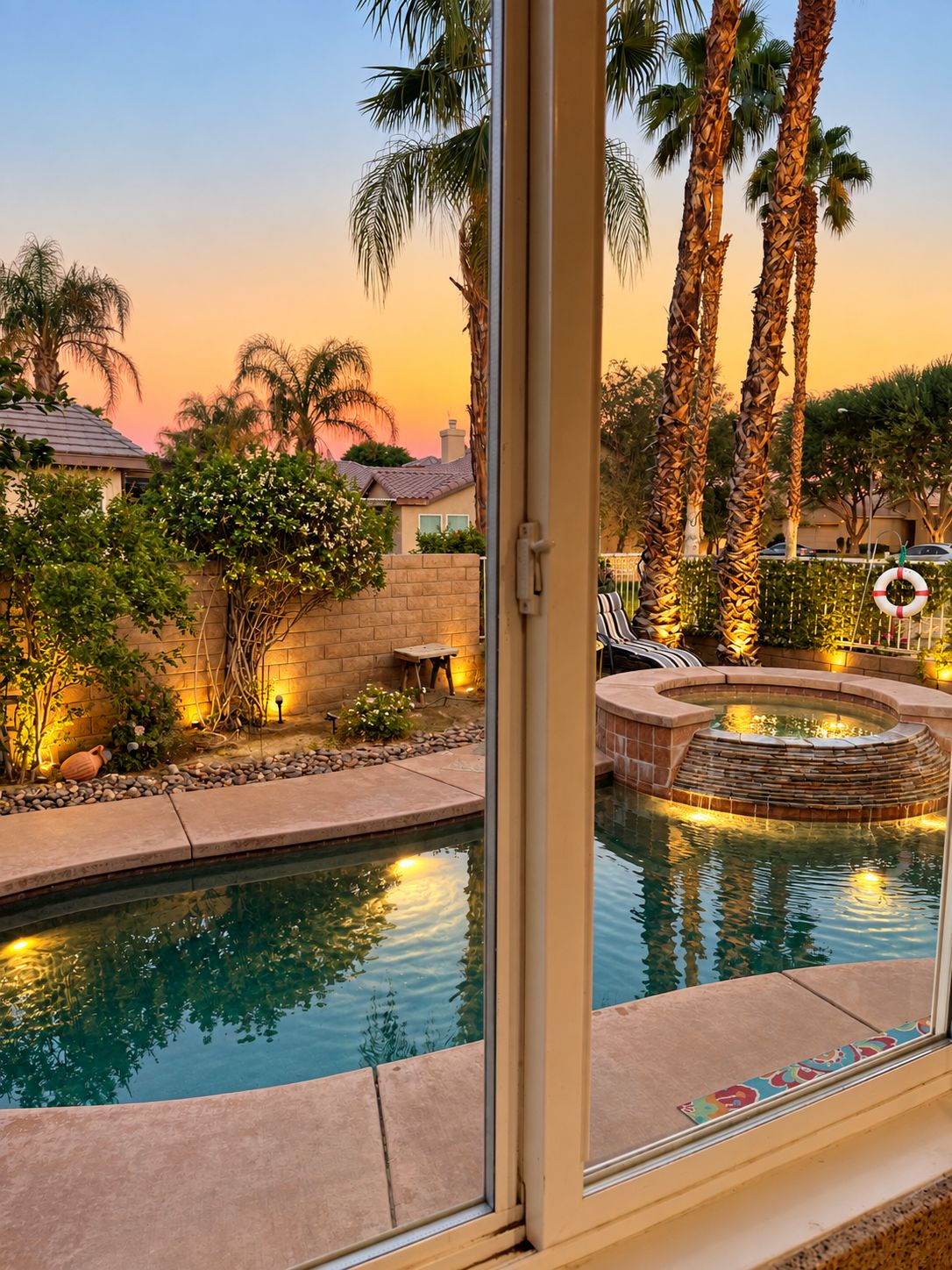 A swimming pool with a stone edge, surrounded by palm trees and a brick wall.