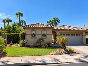 A residential house with a tiled roof, two arched windows, a garage, and a well-maintained lawn with various plants and cacti. - Redford Villa- 3BR Home + 1BR Private Casita, Pool/Spa, Close to Polo (Indio)