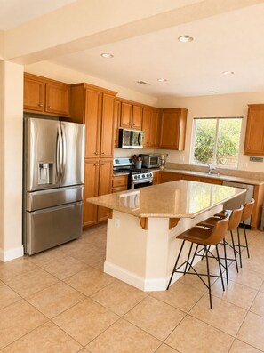 A modern kitchen with a central island, stainless steel appliances, wooden cabinets, and a large window. - Redford Villa- 3BR Home + 1BR Private Casita, Pool/Spa, Close to Polo (Indio)