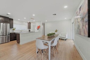 Een moderne keuken met een centraal eiland, witte kasten en een eethoek met een tafel en stoelen.