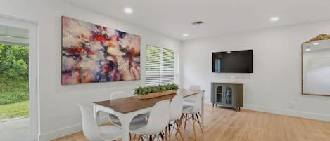 Un coin repas avec une table en bois et des chaises blanches, une grande peinture abstraite, un téléviseur et une cheminée.