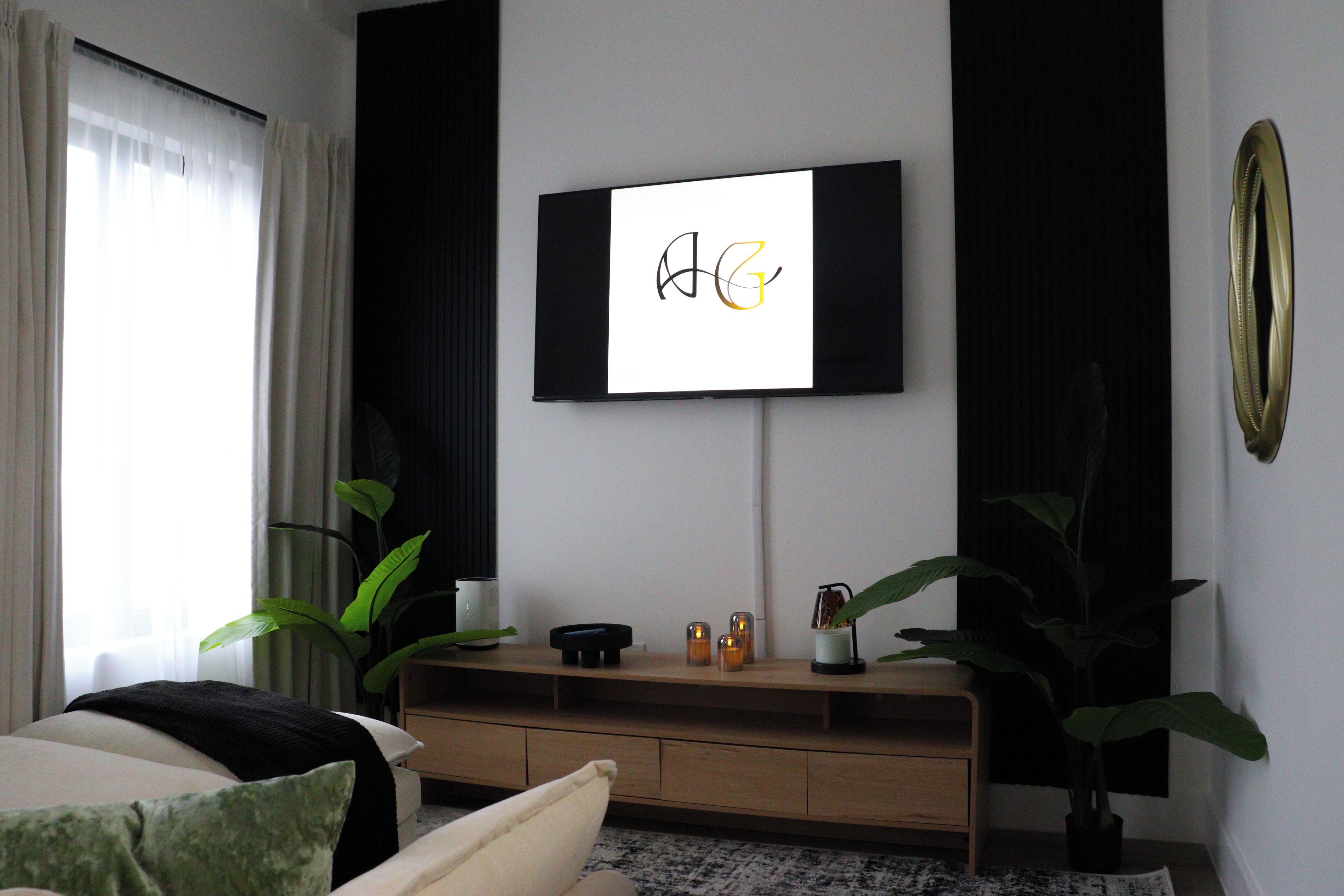 Un salon moderne avec un téléviseur à écran plat fixé au mur, une console en bois et des plantes en pot.