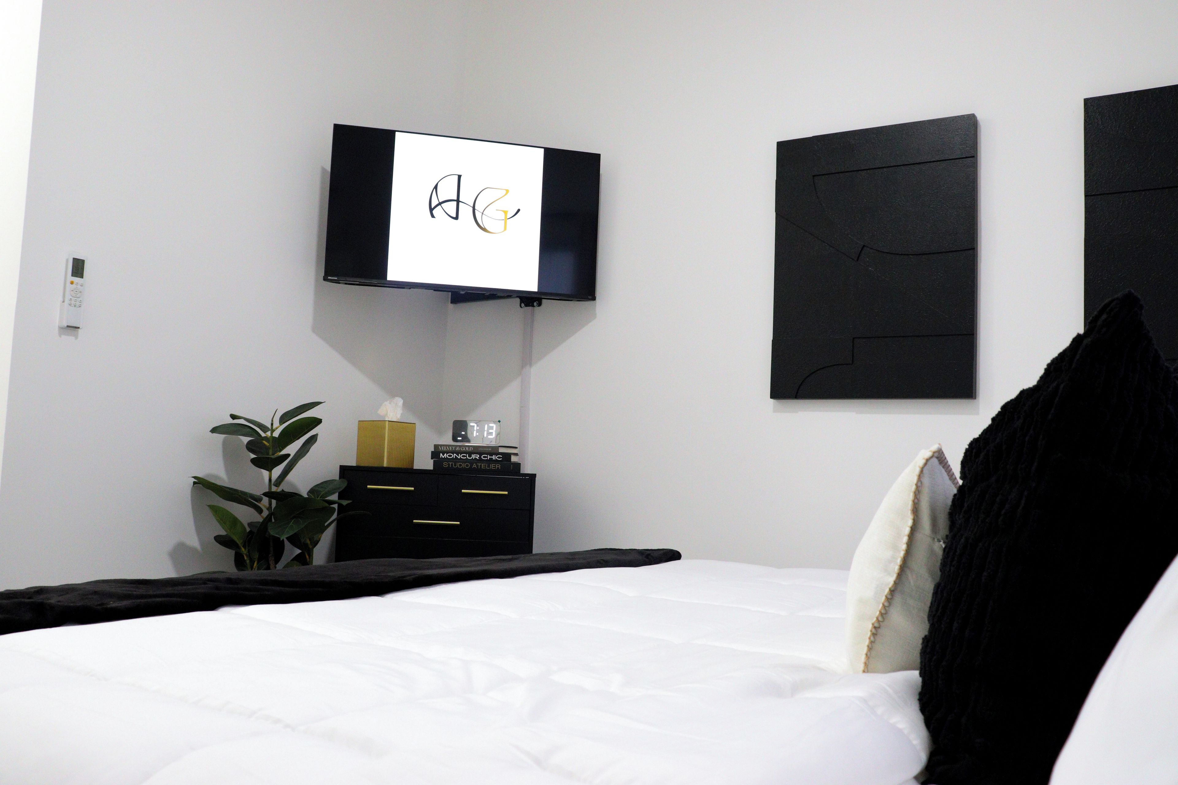 Ein Hotelzimmer mit Bett, Wandfernseher, Nachttisch mit einer Uhr und einer Pflanze.
