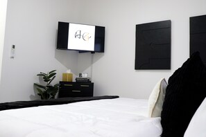 A hotel room with a bed, a TV mounted on the wall, a bedside table with a clock, and a plant. - Stylish Miami Stay Near Brickell & Downtown (Miami)