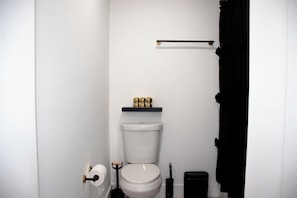 A bathroom with a toilet, a black trash bin, a toilet brush, and a roll of toilet paper. - Stylish Miami Stay Near Brickell & Downtown (Miami)