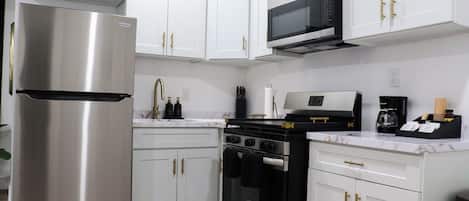 A modern kitchen with stainless steel appliances, white cabinetry, and gold handles.