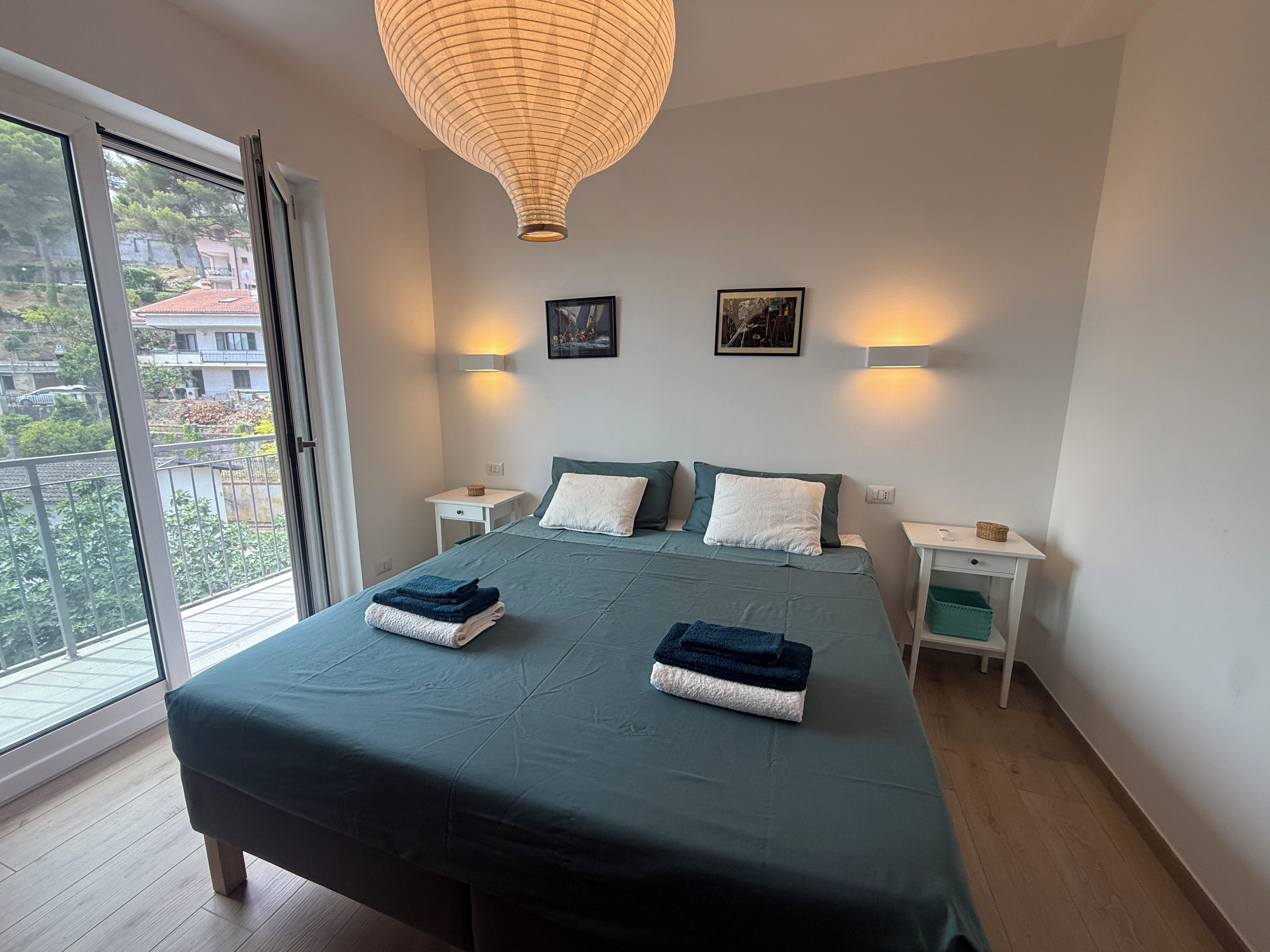 Ein Schlafzimmer mit einem großen Bett, zwei Nachttischen, einer Pendelleuchte und Blick durch ein Fenster.