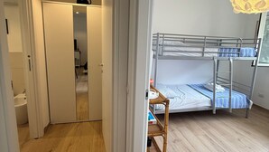 A room with a bunk bed, a wooden floor, a white wardrobe, and a bathroom with a white sink. - Villa Mary - Two Bedroom Apartment, Sleeps 4 (Marina di Andora)