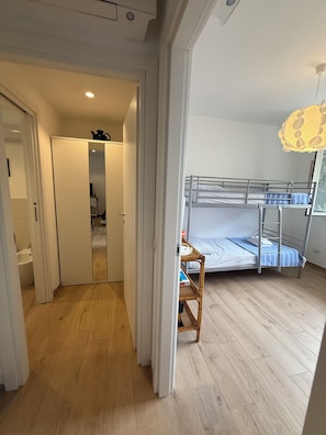 Een kamer met een stapelbed, een houten vloer, een witte garderobe en een badkamer met een wit wastafelmeubel.
