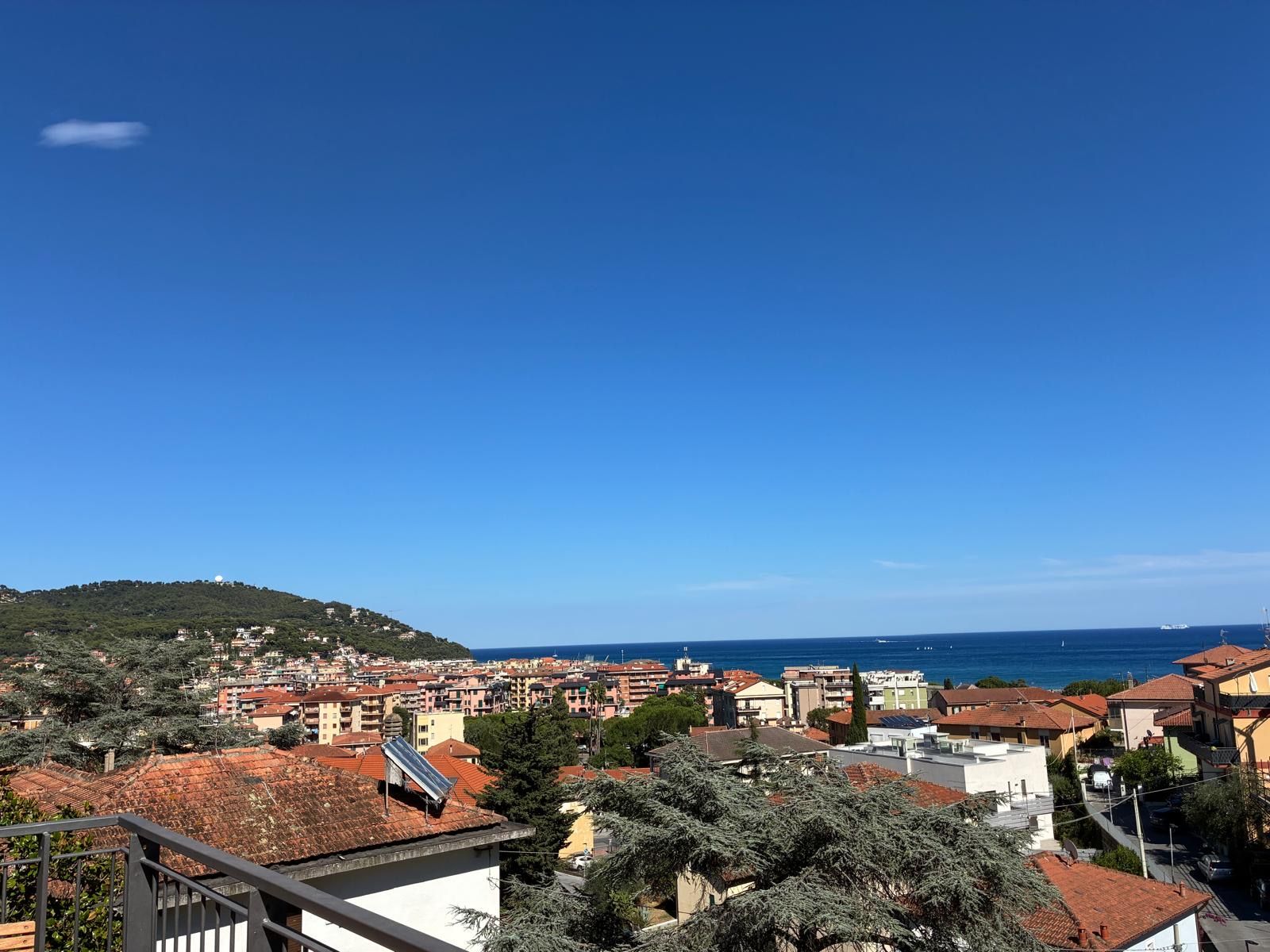 A coastal town with buildings, a hill with a dome structure, and the sea in the background.