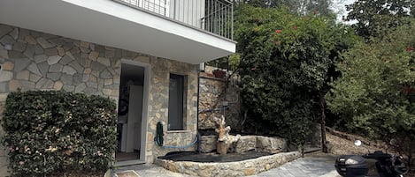 Un edificio de dos pisos con fachada de piedra, un balcón con barandas de metal y un camino de entrada pavimentado.