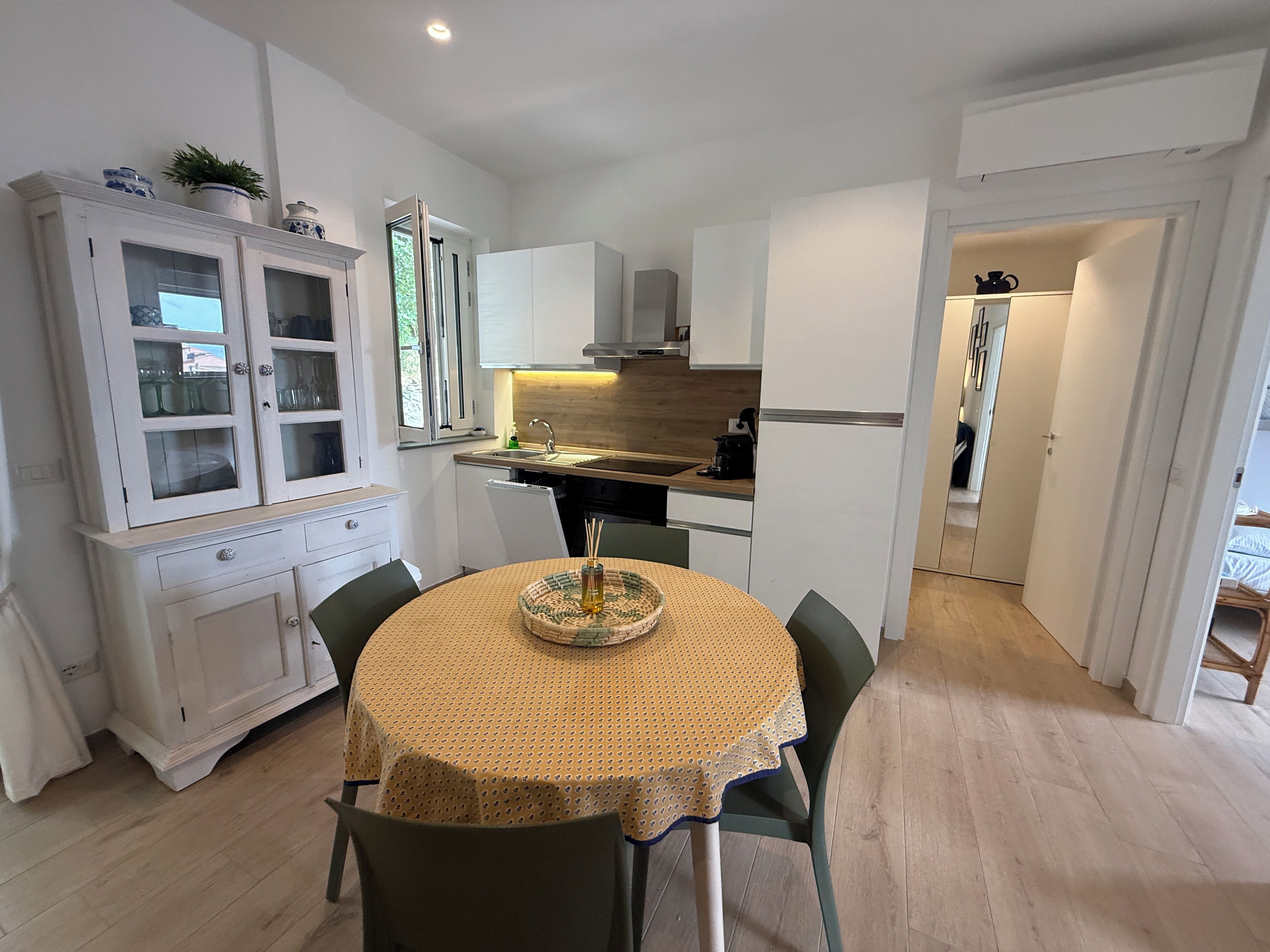Een kleine keuken met witte keukenkastjes, een eettafel met een gele tafelkleed, en een klein schiereiland met een gevlochten mand.