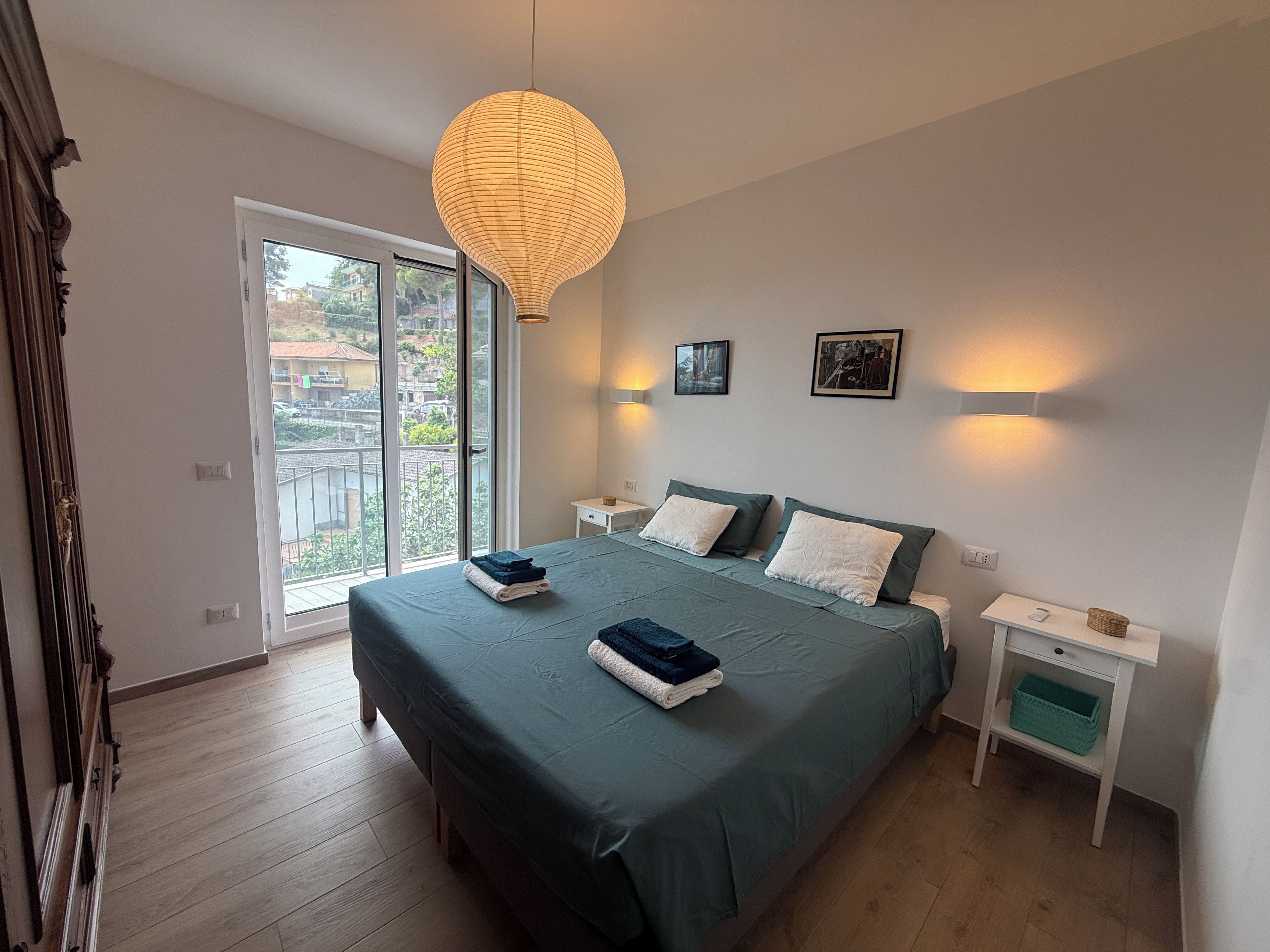 Une chambre à coucher avec un lit, des tables de chevet, un luminaire suspendu et une fenêtre donnant sur un beau paysage.