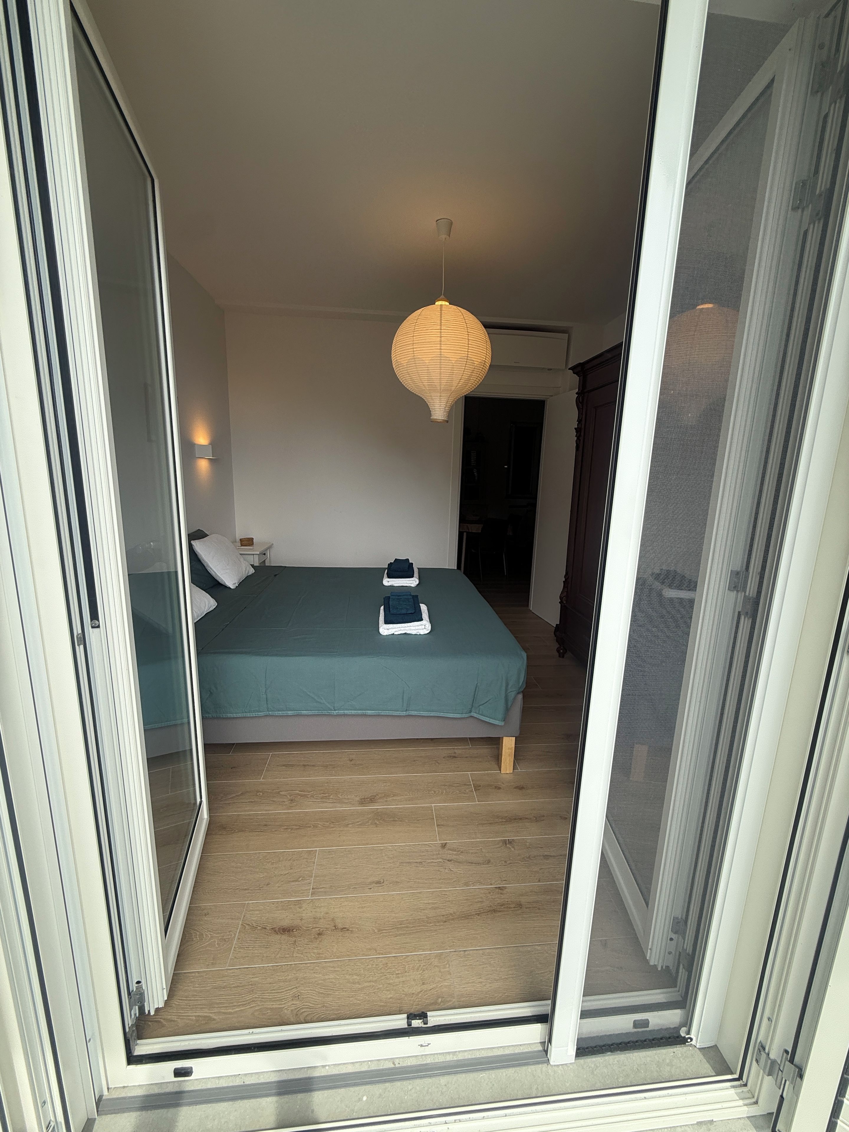 Een slaapkamer met een bed, een nachtkastje, een lamp en een glazen schuifdeur naar een andere kamer.