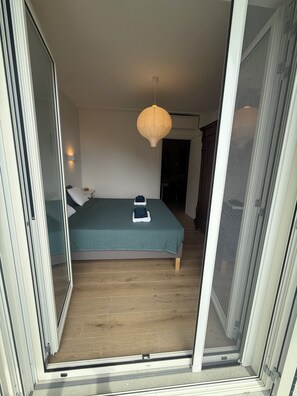 Un dormitorio con una cama, una mesita de noche, una lámpara y un ventanal corredero que da a otra habitación.