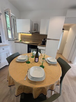 Een moderne keuken met witte kasten, een houten aanrechtblad en een eethoek met een geel tafelkleed met een patroon.