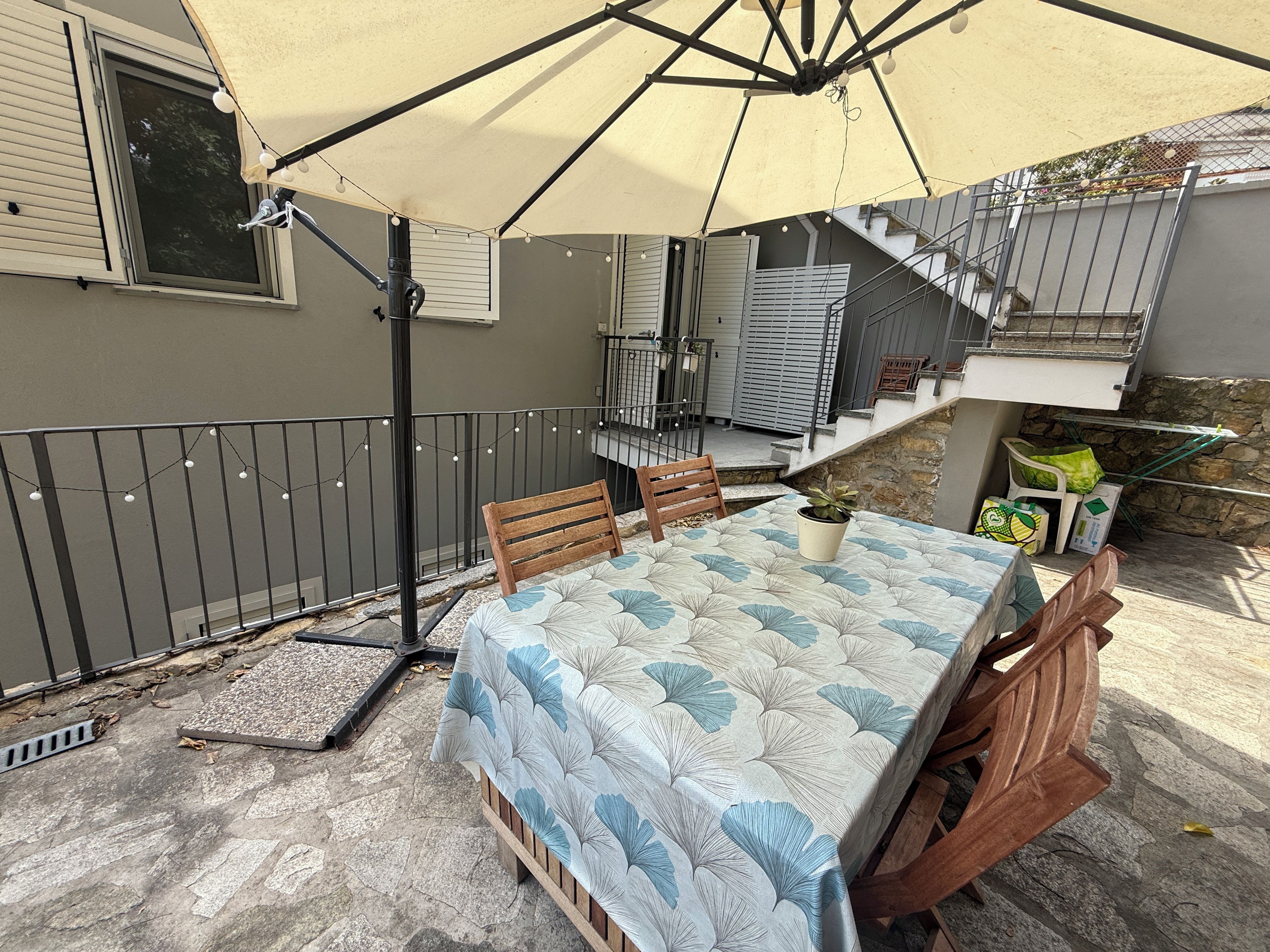 Een terras met een tafel, stoelen, een pergola en een trap naar een hoger gelegen niveau.