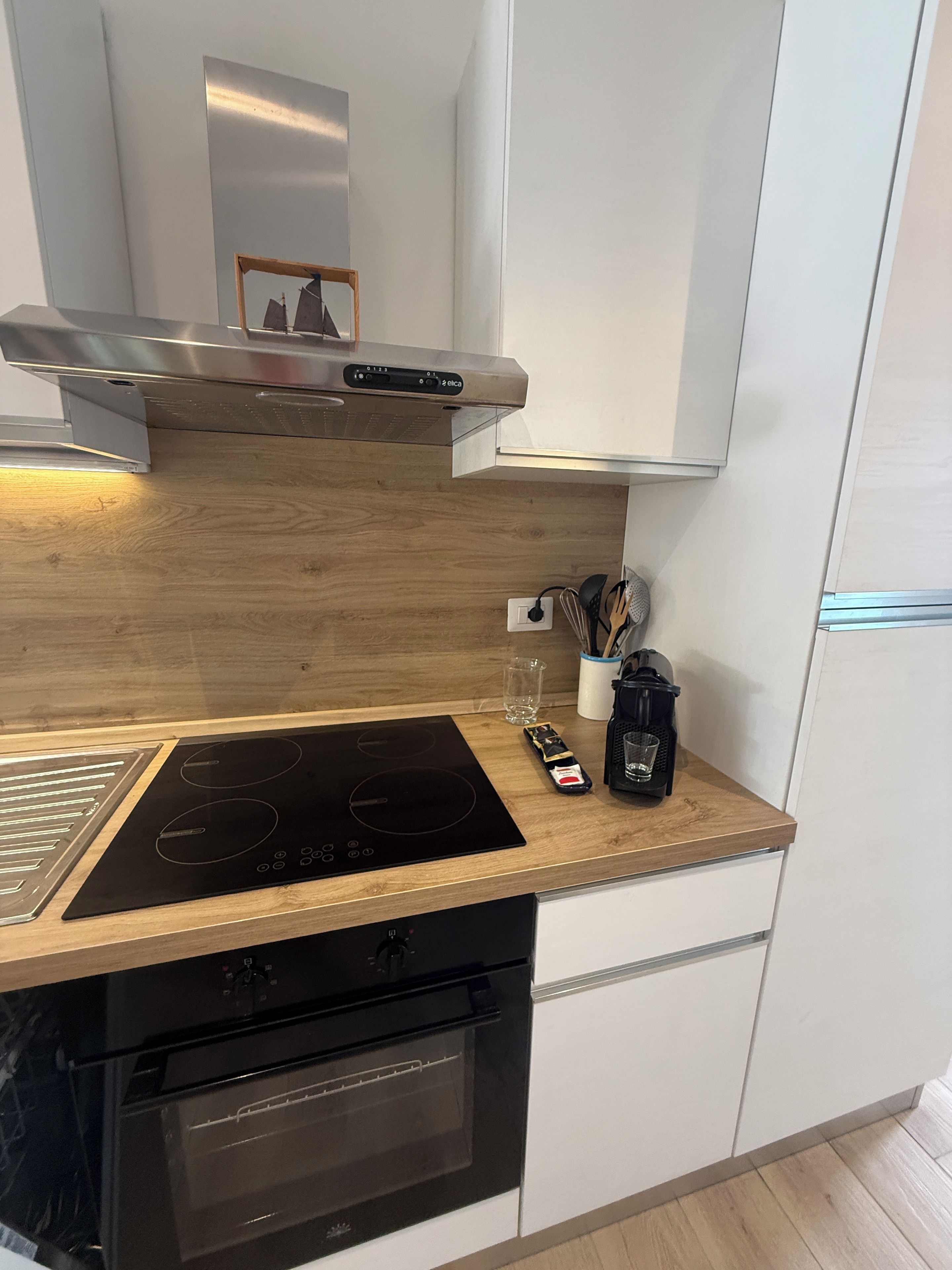 Eine moderne Küche mit einer schwarzen Induktionskochplatte, einem eingebauten Backofen und einer Edelstahl-Dunstabzugshaube.