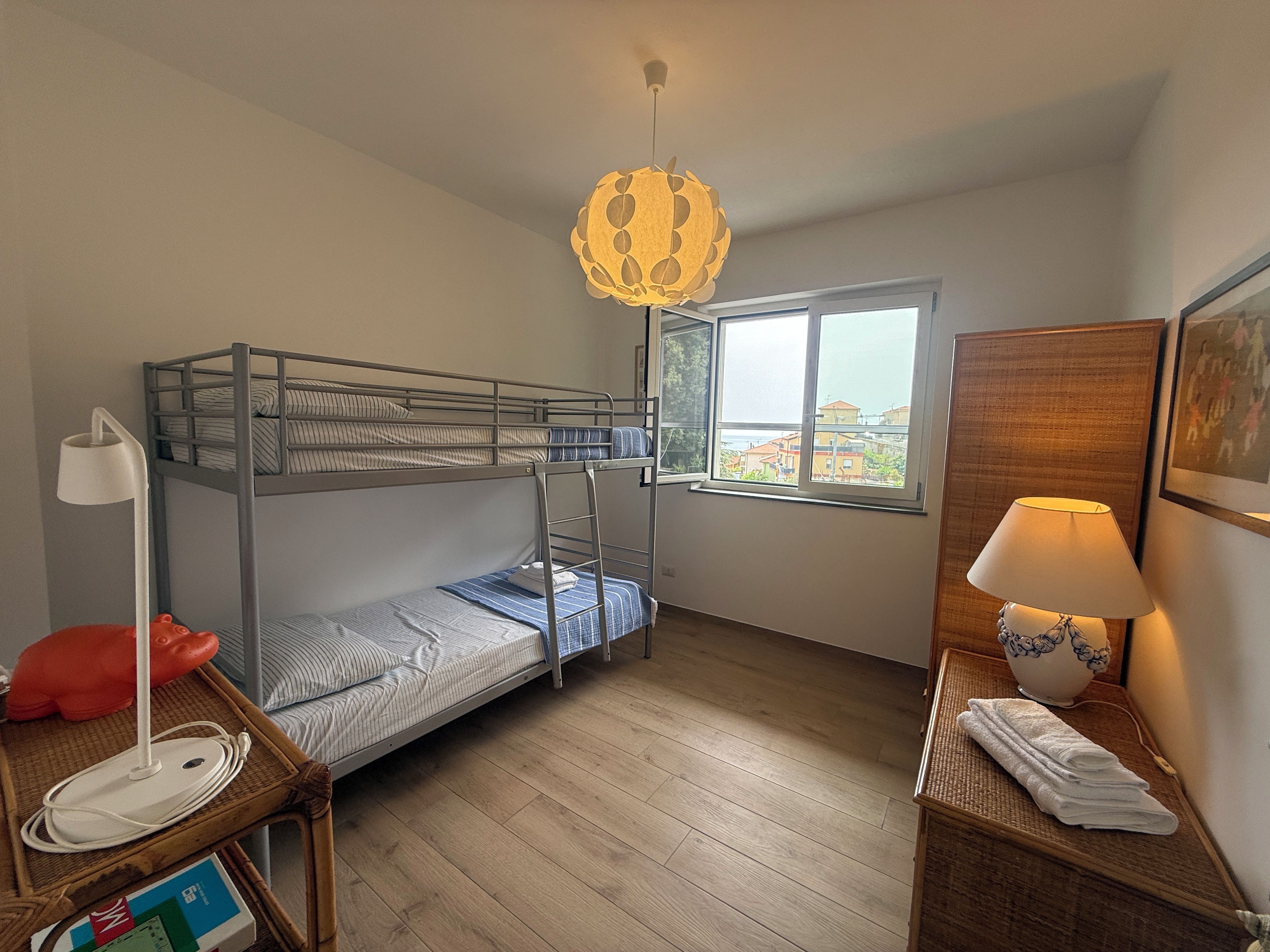 Ein Schlafzimmer mit Etagenbetten, einem Fenster, einem Schreibtisch mit Lampe und einem Nachttisch mit Lampe und Handtüchern.