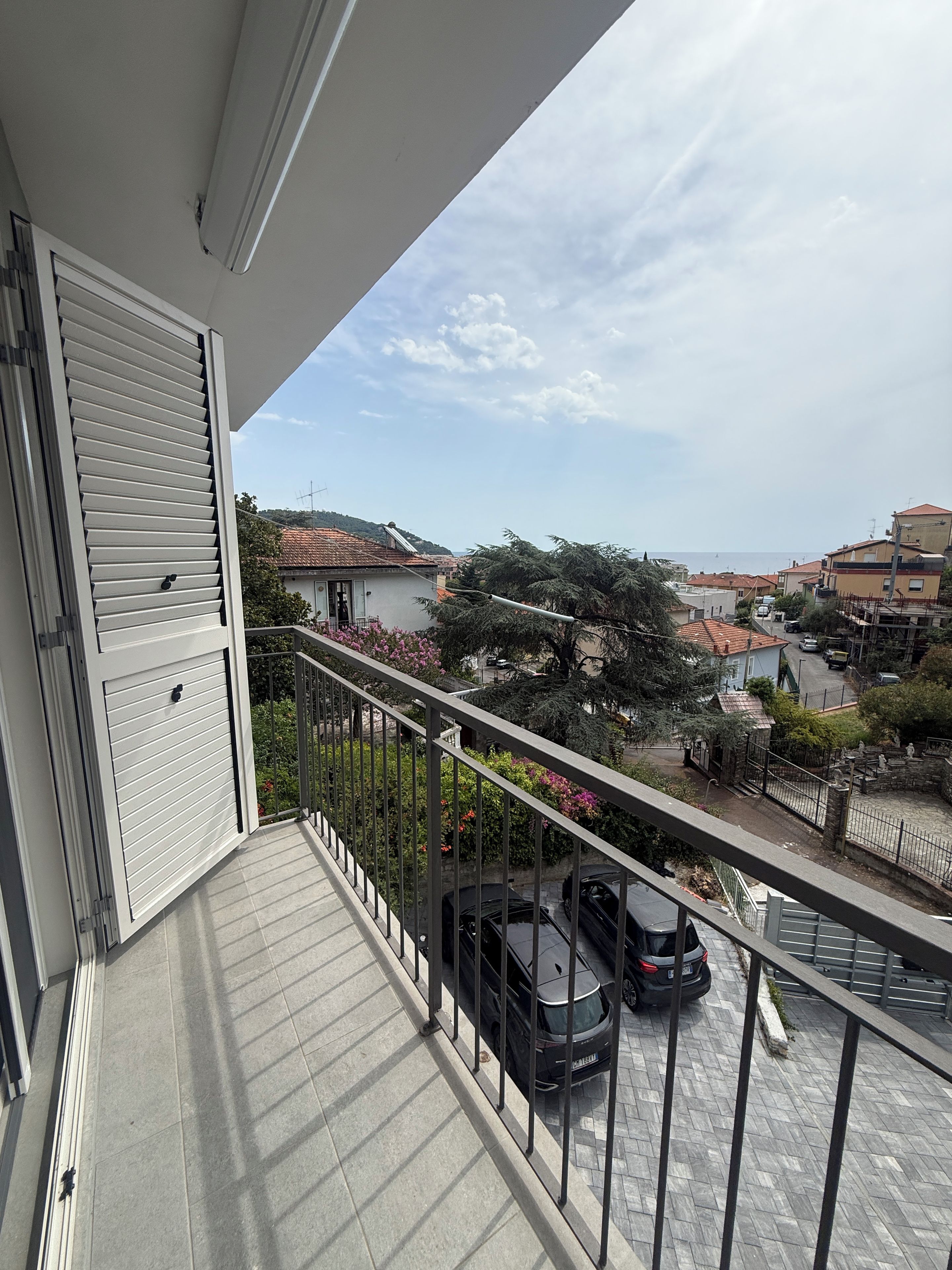 Ein Balkon mit Blick auf ein Wohngebiet, ein geparktes Auto und einen klaren Himmel.
